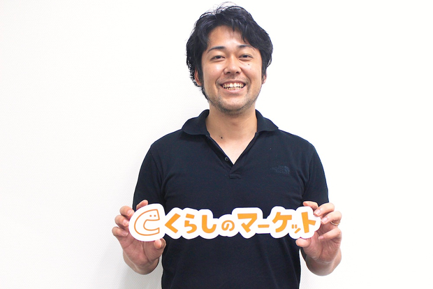 くらしのマーケットのロゴを持って笑う時吉さん