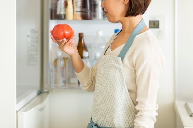 冷蔵庫に入れていたのに凍ってしまったトマトを見つめる主婦
