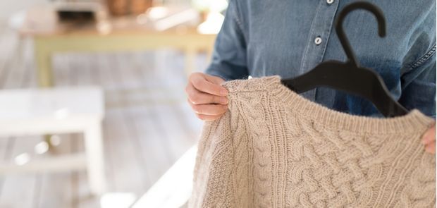 ハンガーにかけられているセーターを女性が持っている
