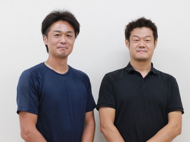 手を組み微笑む男性2人