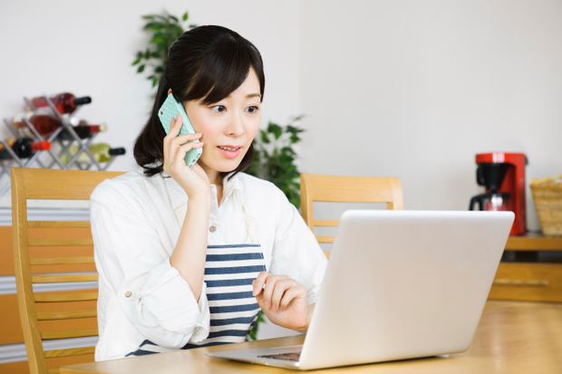 パソコンを見ながら電話をする女性