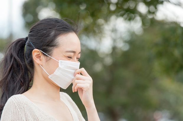 マスクをつけたくしゃみを我慢する女性