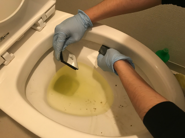 鏡を使って便器のフチの中をやすりで掃除する様子