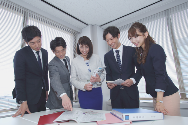 オフィスのデスクに集まり話し合う社員達